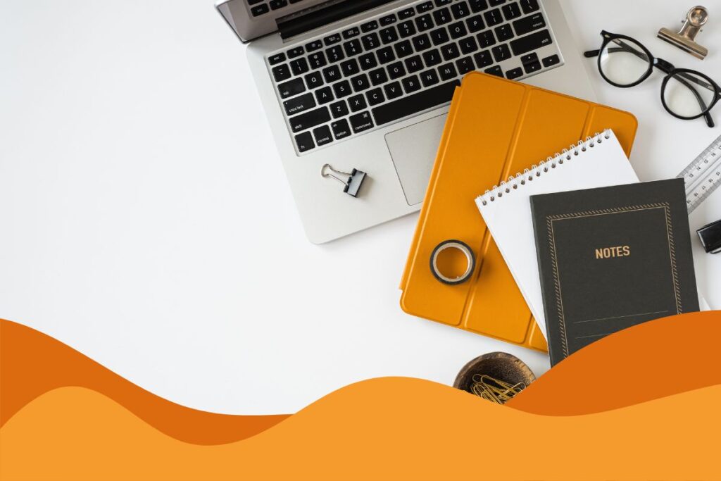 A laptop, tablet with an orange case and a notepad on a desk, symbolising employee cybersecurity training.