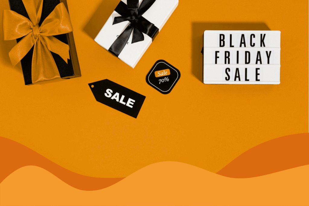 orange background with black friday bold text on white block, with presents surrounding it and multiple sale tags from a birds eye view in a n article about how to stay safe shopping this black friday