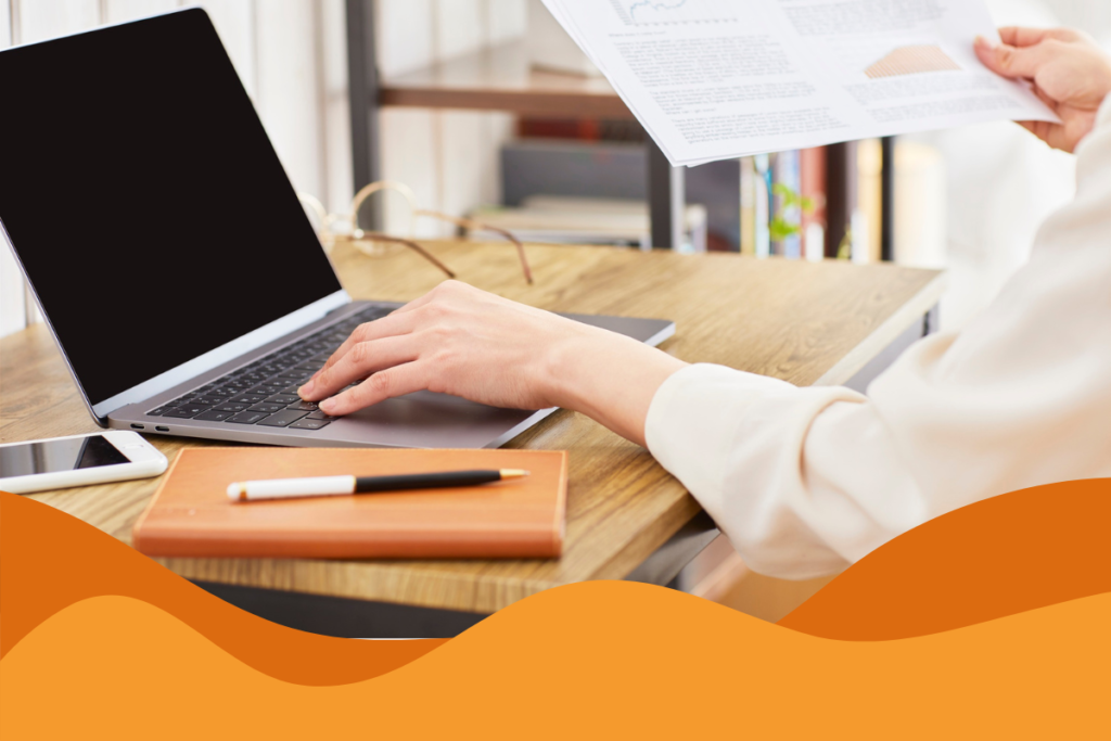 image of a woman wearing a white long sleeve on her laptop with a dark screen, also holding paperwork and with a book at the desk in an article about how strong it support improves employee productivity