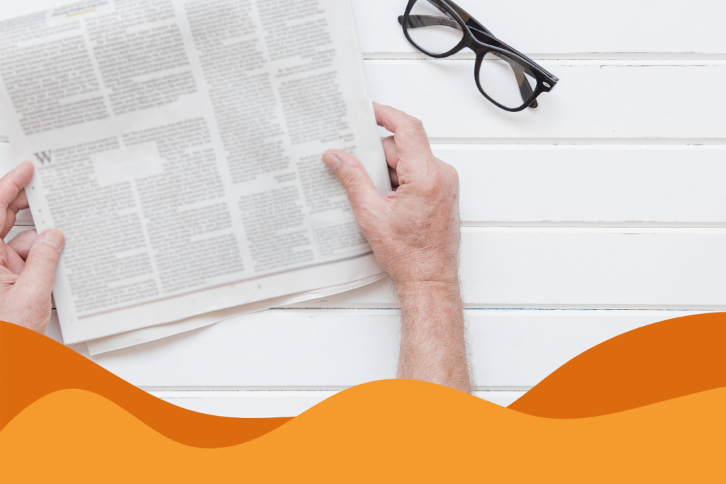 Image of a man reading a white newspaper on a white panelled surface with black glasses next to him in an article of Daffodil IT news roundup