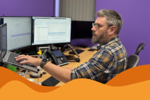 An image of an IT Projects Engineer working on laptop at desk in front of a purple wall at Daffodil IT, IT MSP in Sheffield, South Yorkshire, in an article explaining June's latest news updates and how to stay cyber safe in South Yorkshire.